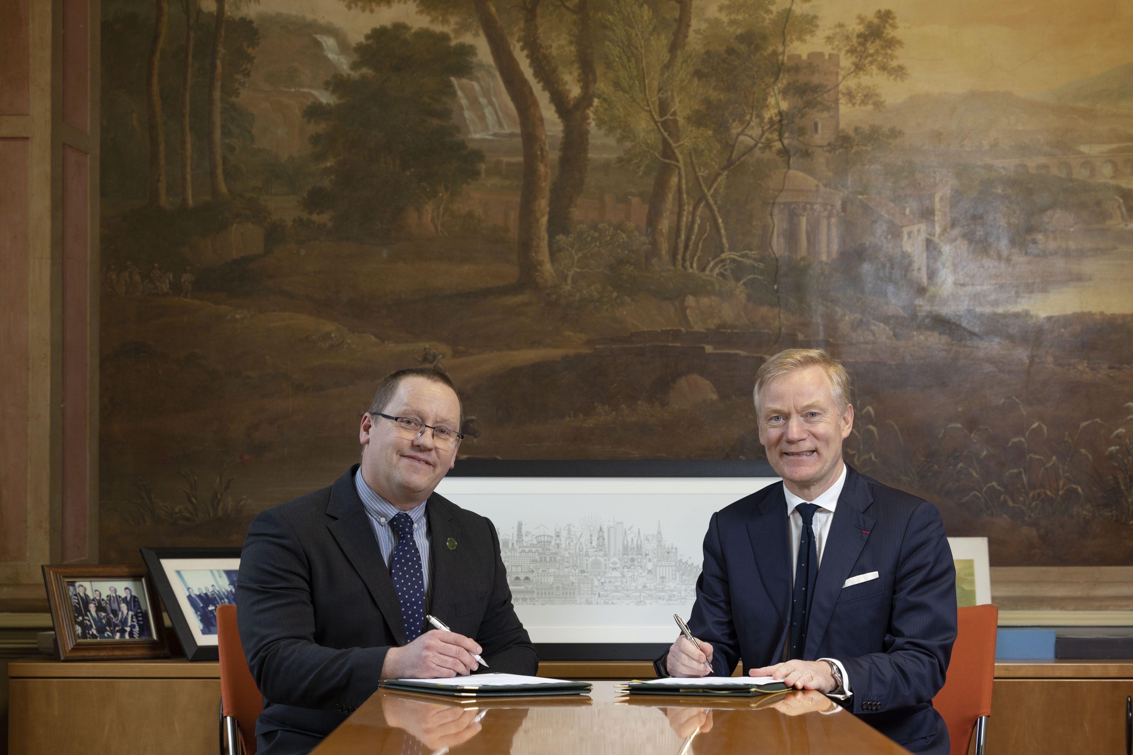 Dr Patrick O'Leary and H.E. Vincent Guérend sitting at a desk in the Registrar's Office of NUI, signing the memorandum of understanding in relation to the NUI - French Embassy collaborative grant.